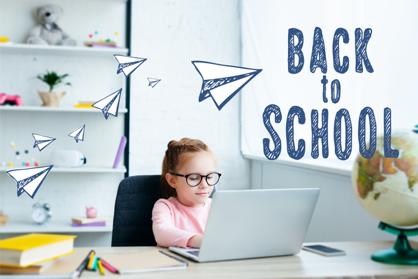 Gyönyörű vörös hajú iskolás használ laptop, miközben tanul otthon Papírrepülők és a "vissza az iskolába" felirat - Fotó, kép