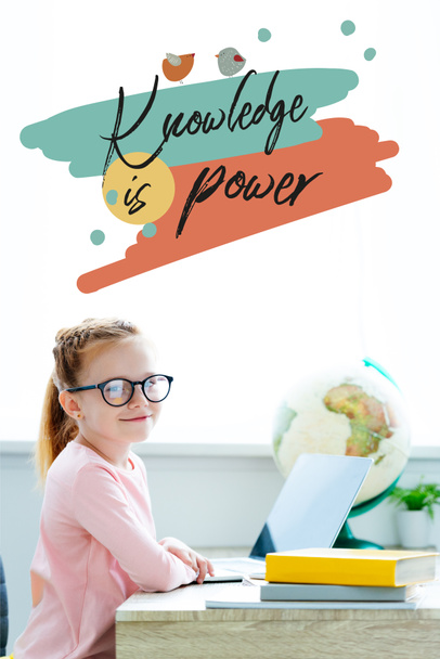 schöne rothaarige Schülerin mit Brille, die während des Lernens mit Büchern und Laptop in die Kamera lächelt, mit dem Schriftzug "Wissen ist Macht" - Foto, Bild