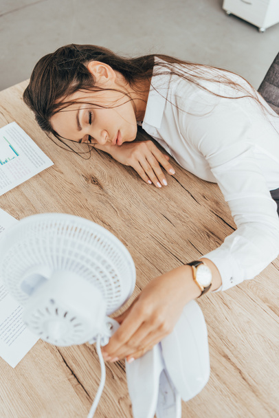 vyčerpaná podnikatelka foukání na sebe s elektrickým ventilátorem v úřadu - Fotografie, Obrázek