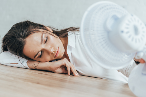 exhausted businesswoman with closed eyes blowing at herself with electric fan in office - Photo, Image
