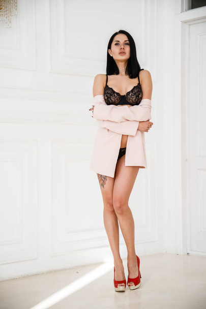 Fashion studio shot of beauty brunette woman with tattoo on body. Beautiful female model in stylish black lingerie standing in luxury apartments interior - Foto, immagini