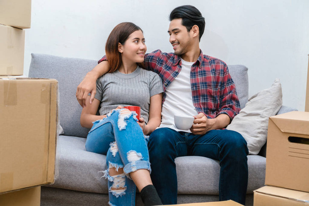 Asiática joven pareja Sentado en el sofá y beber para relajarse después de éxito embalaje caja de cartón grande para mudarse en nueva casa, Mudanza y casa concepto de caza
 - Foto, imagen