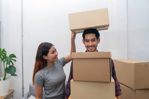 Asiática joven pareja llevando gran caja de cartón para moverse en nueva casa, Ayudando a reubicarse y bromeando juntos, Mover y casa concepto de caza
 - Foto, Imagen