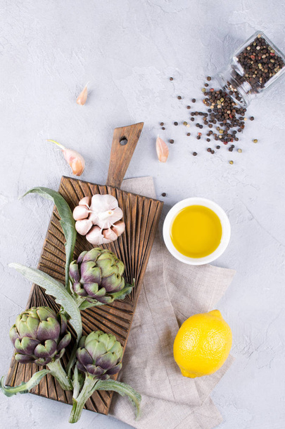 Fresh ripe green artichokes on cutting board ready to cook and ingredients garlic, lemon and olive oil - Fotoğraf, Görsel