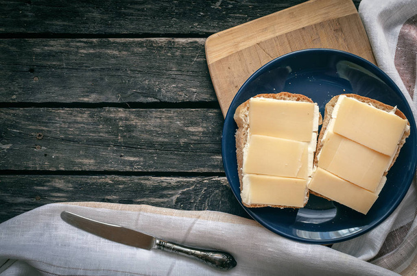 Panino con formaggio e burro sul piatto blu. Cucina rustica. Colazione semplice. Fast food
. - Foto, immagini