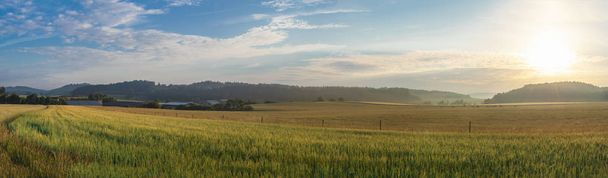 Красочная панорама с восходом солнца над пастбищами, зерновыми полями, холмами, лесами и современной фермой с солнечными батареями, в районе Баден Вюртемберг, Германия
. - Фото, изображение