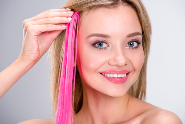 happy young woman applying pink clip-on hair strand isolated on grey - Foto, Imagem