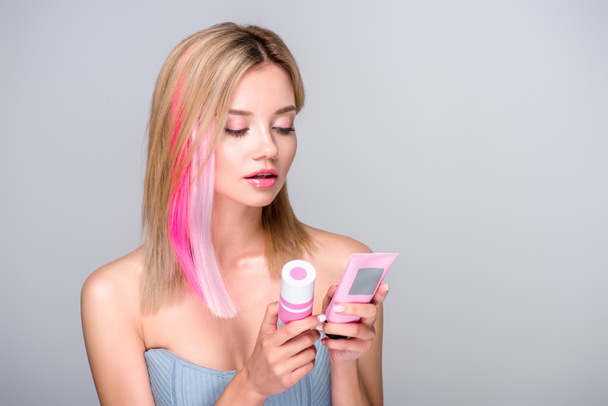 schöne junge Frau mit farbigem Bob-Schnitt hält Haarpflegemittel isoliert auf grau - Foto, Bild
