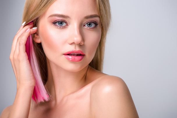 close-up portrait of beautiful young woman putting colored hair behind ear and looking at camera isolated on grey - Фото, изображение