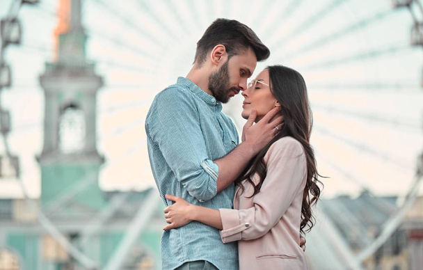 Love is in the air! Cute romantic couple spending time together in the city. Handsome bearded man and attractive young woman are in love. Hugging, kissing and having fun on the Ferris wheel background. - Foto, Bild