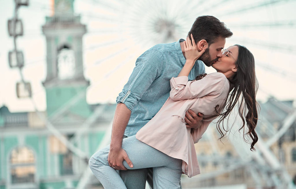 Love is in the air! Cute romantic couple spending time together in the city. Handsome bearded man and attractive young woman are in love. Hugging, kissing and having fun on the Ferris wheel background. - Foto, imagen