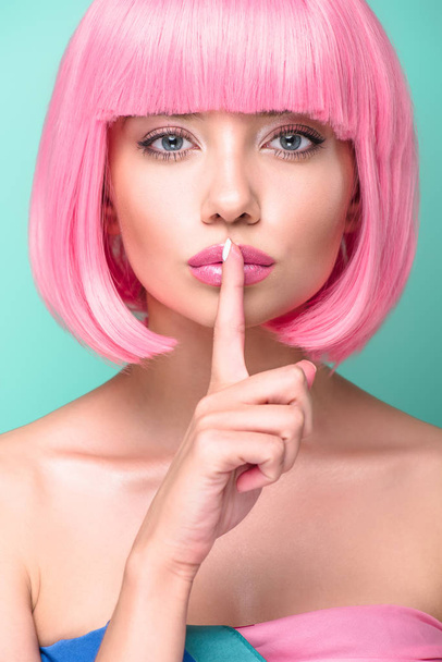 close-up portrait of young woman with pink bob cut showing silence gesture and looking at camera isolated on turquoise - Photo, Image