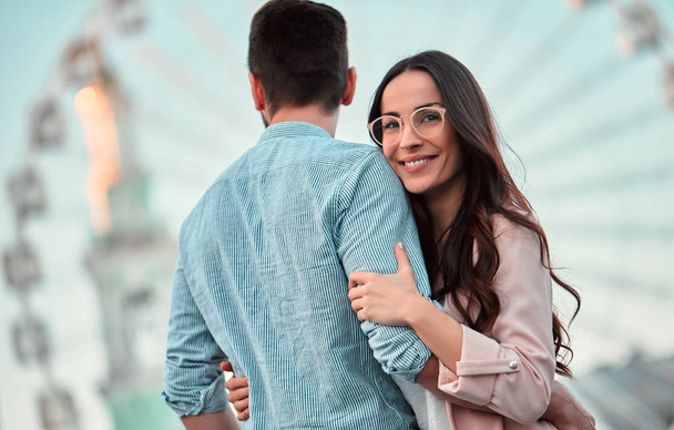 Love is in the air! Cute romantic couple spending time together in the city. Handsome bearded man and attractive young woman are in love. Hugging, kissing and having fun on the Ferris wheel background. - Foto, Imagem