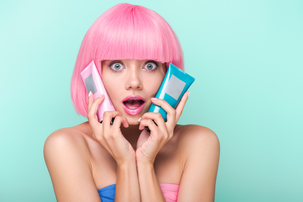 shocked young woman with tubes of coloring hair tonics looking at camera isolated on turquoise - Photo, Image