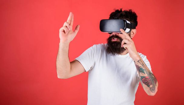 Man with beard in VR glasses shooting, red background. Virtual shooting gallery concept. Guy with head mounted display shoot with gun in virtual reality. Hipster on busy face play in virtual reality - Foto, immagini