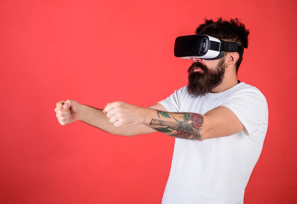 Virtual racing concept. Man with beard in VR glasses driving car, red background. Hipster on concentrated face driving car on high speed in virtual reality. Guy play racing game in VR - Foto, Imagem