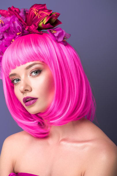attractive young woman with pink bob cut and flowers in hair looking at camera isolated on violet - Fotografie, Obrázek