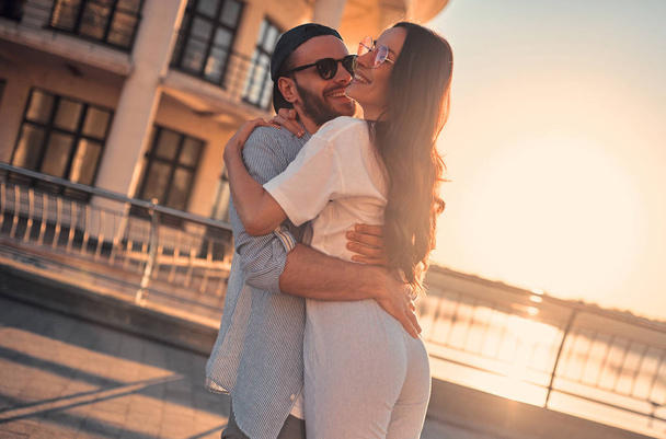 Love is in the air! Cute romantic couple spending time together in the city. Handsome bearded man and attractive young woman are in love. Hugging, kissing and having fun during the sunset. - 写真・画像