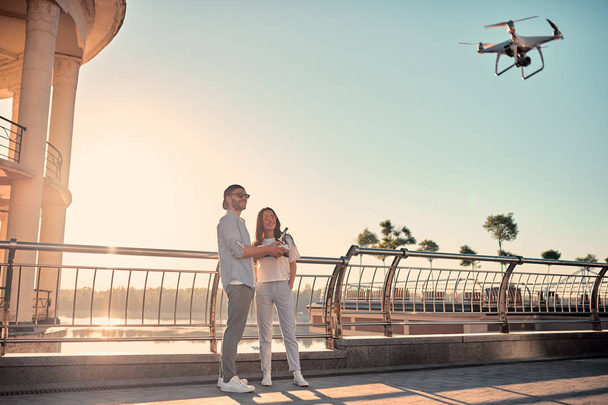 Love is in the air! Cute romantic couple spending time together in the city with quadrupter. Handsome bearded man and attractive young woman are in love. Couple with drone during sunset. - Foto, imagen