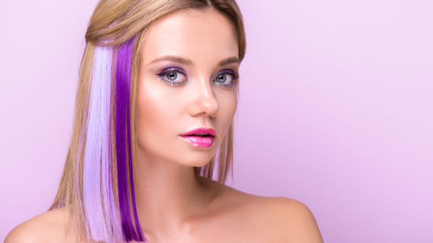 close-up portrait of beautiful young woman with stylish makeup and purple hair strands looking at camera isolated on purple - Fotografie, Obrázek