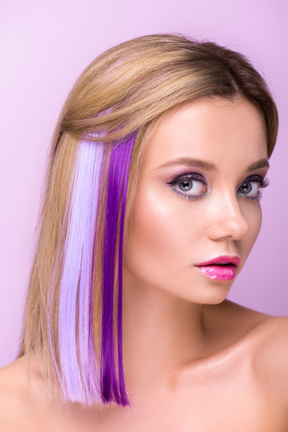 close-up portrait of attractive young woman with stylish makeup and purple hair strands looking at camera isolated on purple - Photo, Image