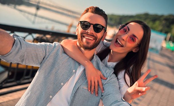 Love is in the air! Cute romantic couple spending time together in the city and making selfie. Handsome bearded man and attractive young woman are in love. Hugging, kissing and having fun during the sunset. - Foto, Imagen