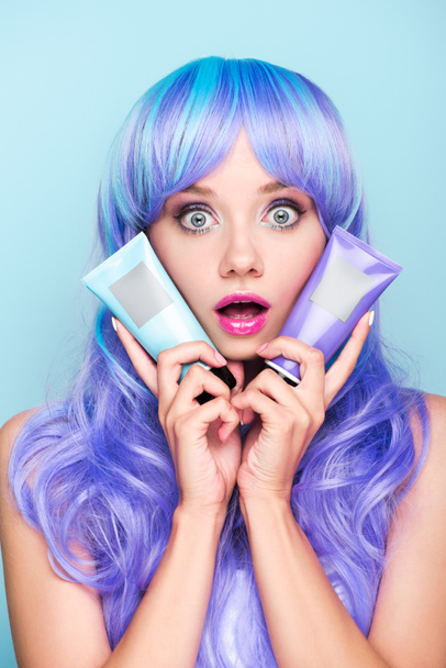 scioccato giovane donna con tubi di coloranti tonici per capelli isolati su blu
 - Foto, immagini