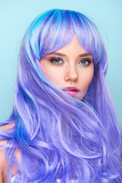 close-up portrait of beautiful young woman with curly blue hair looking at camera isolated on blue - Foto, Imagem