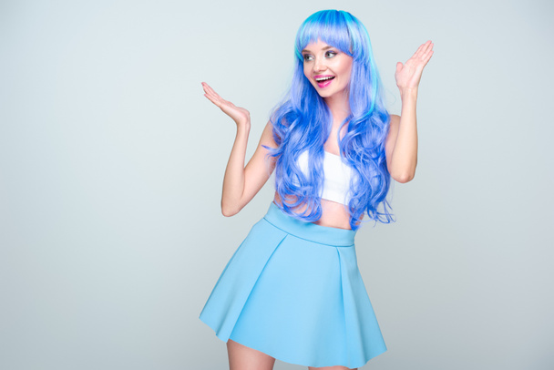 enthousiast jonge vrouw met helder blauwe haar en verhoogde handen geïsoleerd op grijs - Foto, afbeelding