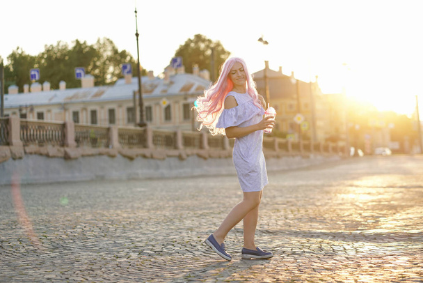  Mavi yaz elbise giymiş pembe saçlı güzel kız şehirde bir cam ile şafak elinde yürür - Fotoğraf, Görsel