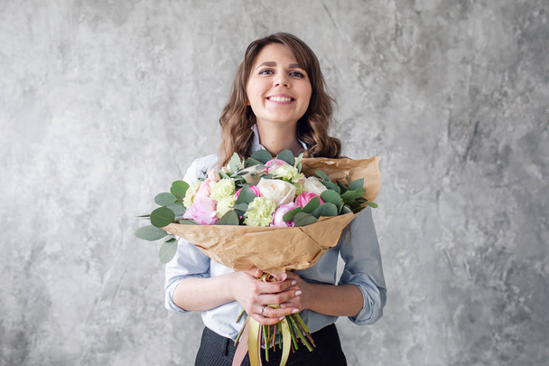 Young Woman looking at the camera, holds a luxurious bouquet in his hands. florist creating beautiful bouquet in flower shop. Girl assistant or owner in floral design studio. - Photo, image