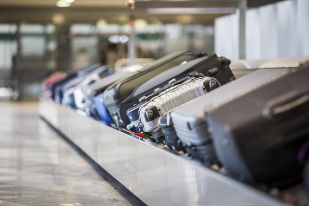 Колесный чемодан и сумки на багажном поясе в терминале аэропорта
. - Фото, изображение