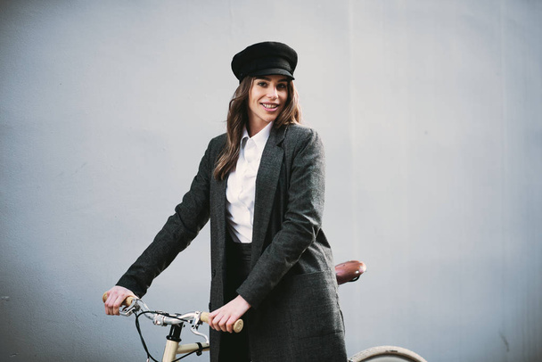 Meisje holding yelloe fiets voor grijze muur. - Foto, afbeelding