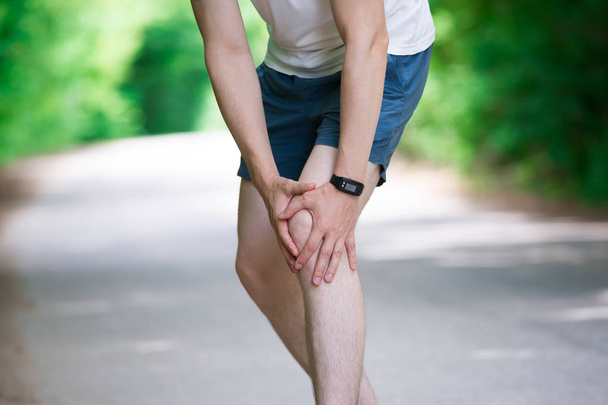 Pain in knee, joint inflammation, massage of male leg, injury while running, trauma during workout, outdoors concept - Photo, Image