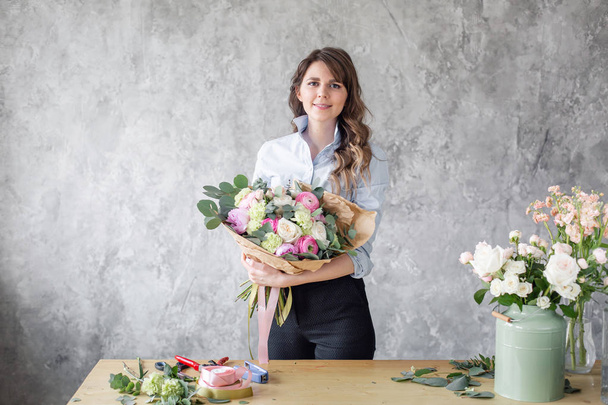 Young Woman looking at the camera, holds a luxurious bouquet in his hands. florist creating beautiful bouquet in flower shop. Girl assistant or owner in floral design studio. - Photo, Image