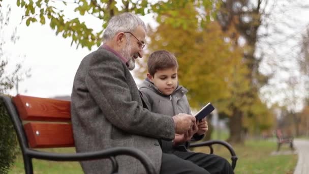 Nagyapa és unokája időt együtt a parkban. Ül a padon, és használja a tabletta - Felvétel, videó