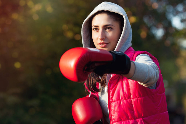 Portrait of a beautiful girl in red boxing gloves. Makes a punch hand - Photo, Image