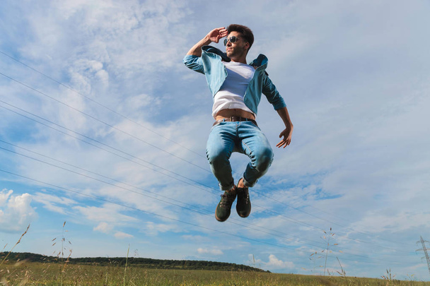 rento mies yllään denim paita ja farkut ja aurinkolasit hypätä kentällä ja näyttää etäisyydeltä
 - Valokuva, kuva