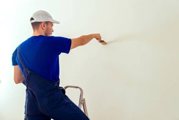 Schilder man op de ladder is schilderen muur in zijn kamer in het wit met penseel - Foto, afbeelding