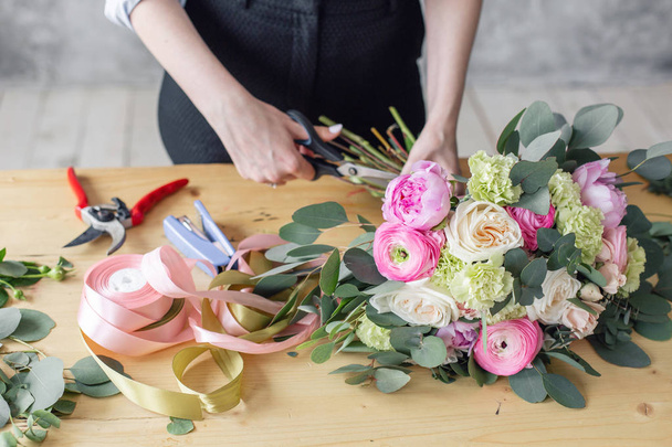 Woman florist creating beautiful bouquet in flower shop. Working in flower shop. Girl assistant or owner in floral design studio, making decorations and arrangements. - 写真・画像