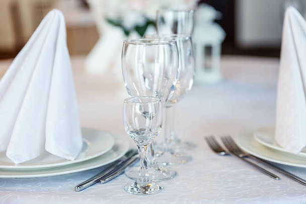 Gläser, Serviette gefaltet in einer Pyramide, serviert zum Abendessen im Restaurant mit gemütlichem Interieur. Hochzeitsdekorationen und Lebensmittel, arrangiert vom Catering-Service auf einem großen Tisch mit weißer Tischdecke - Foto, Bild