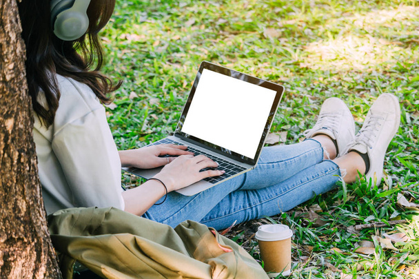 Nainen rentoutua ja käyttää kannettavaa tietokonetta istuu nurmikolla puistossa
 - Valokuva, kuva
