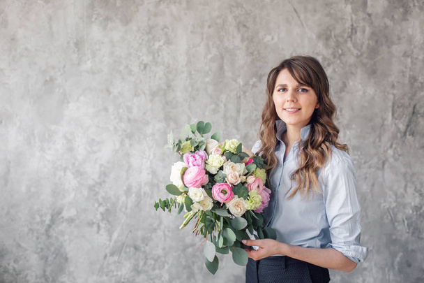 Young Woman looking at the camera, holds a luxurious bouquet in his hands. florist creating beautiful bouquet in flower shop. Girl assistant or owner in floral design studio. - Fotó, kép