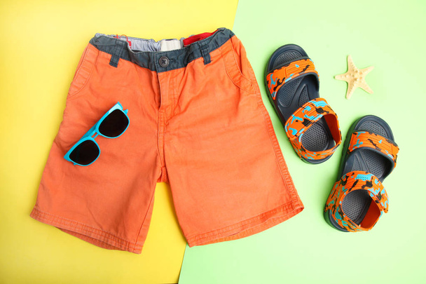 Pantalones cortos y sandalias de verano para niños sobre un fondo amarillo y verde, vista superior
 - Foto, Imagen