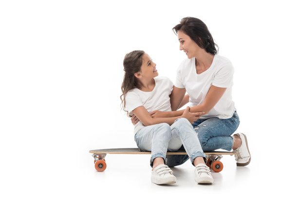 mother sitting near smiling daughter on skateboard isolated on white - Fotografie, Obrázek