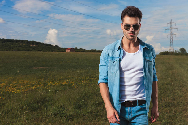 portrait of casual man with sunglasses standing on a field in the countryside, in daylight - Photo, Image