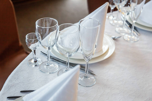 Glasses,  napkin folded in a pyramid, served for dinner in restaurant with cozy interior. Wedding decorations and items for food, arranged by the catering service on a large table covered with white tablecloth - Photo, Image