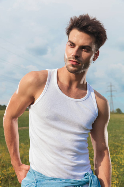 retrato de homem casual atraente em camiseta branca em pé no campo de grama olhando para o lado
 - Foto, Imagem