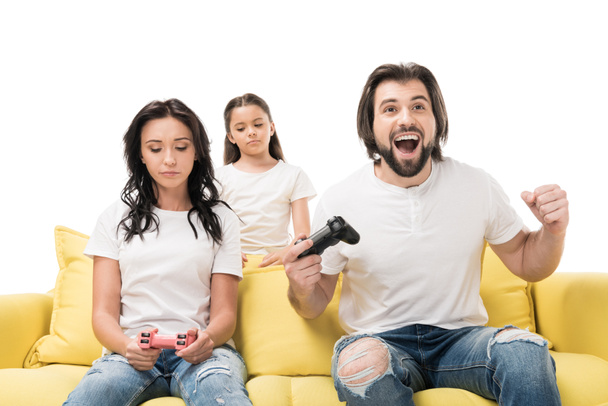 glücklicher Mann und verärgerte Familie beim Spielen von Videospielen auf gelbem Sofa isoliert auf weißem Grund - Foto, Bild