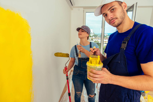 Piękna para malarstwo wnętrze domu w kolorze żółtym z rolką pędzel i farby - Zdjęcie, obraz